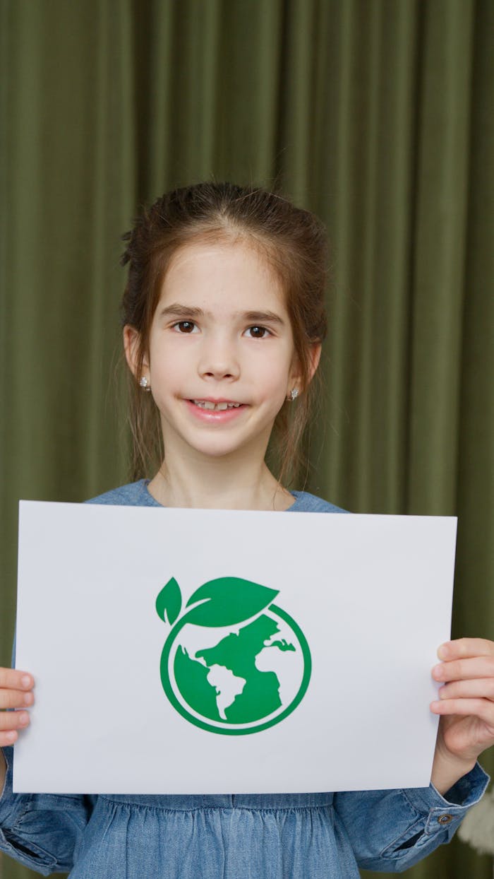 Young girl in blue dress holding eco-friendly Earth symbol poster indoors.