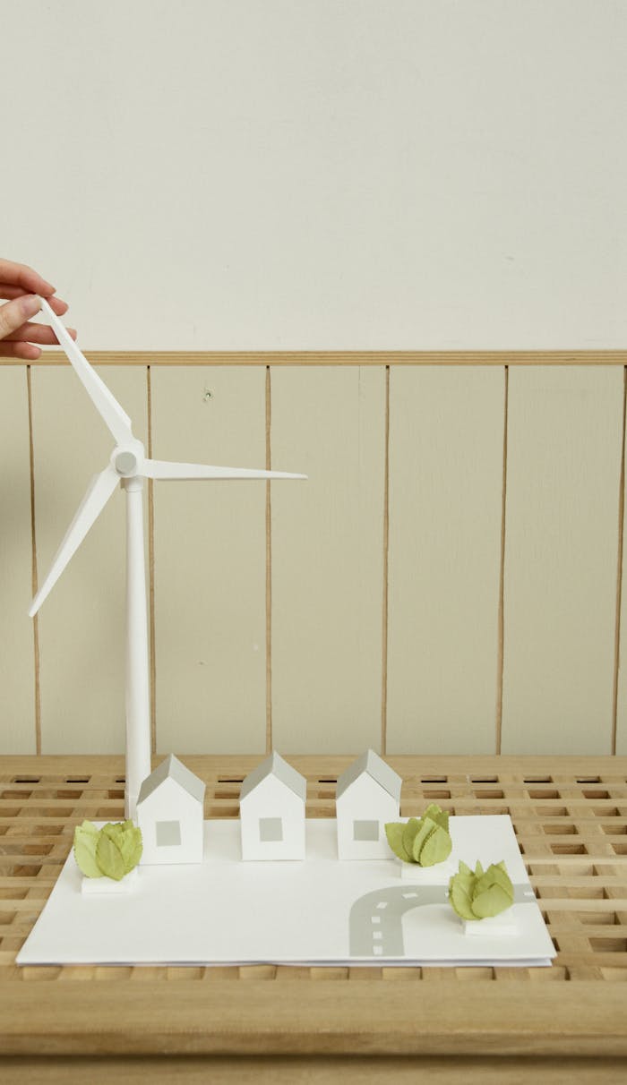 Paper model showcasing sustainable energy with a wind turbine, houses, and greens on a wooden surface.