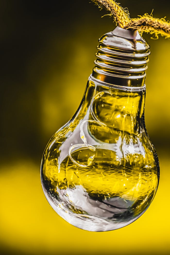 about-02 A clear glass light bulb hanging on a textured rope against a vibrant yellow backdrop.